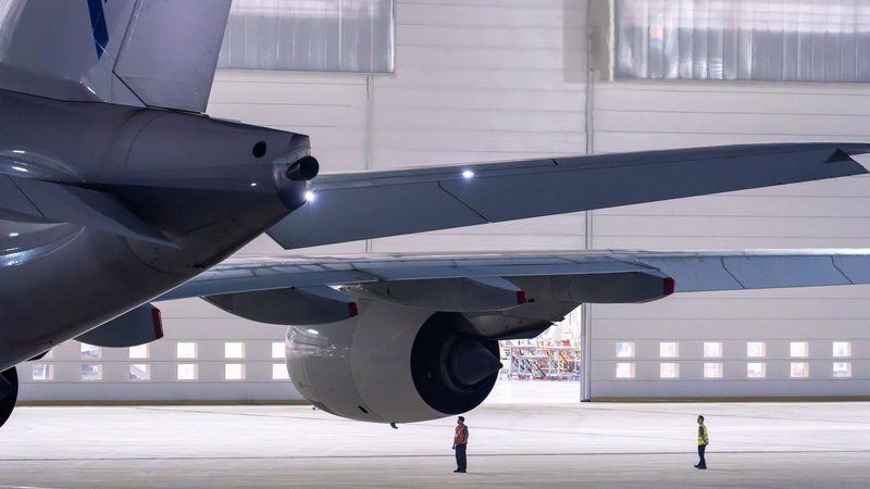Wide-body aircraft in a maintenance hangar with ground crew working beneath the wing