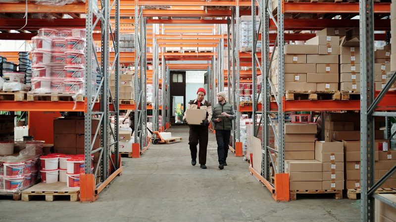 Warehouse workers handling a package among shelves of stock